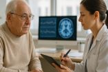 Una especialista en salud mental realiza una evaluación neuropsicológica a un hombre mayor en un consultorio médico. En el fondo, se observa una imagen cerebral en una pantalla de computadora, lo que indica un análisis detallado de funciones cognitivas para detectar posibles signos de demencia.