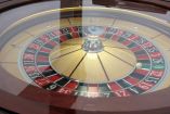 Una ruleta de casino vista desde arriba, con la bola detenida en un número rojo, bajo una cubierta de cristal. Este tipo de juegos de azar tradicionales sirven como modelo para mecánicas similares en videojuegos dirigidos a adolescentes, como cajas de botín y ruletas virtuales.
