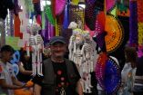 Kim Manresa en un mercado del Día de Muertos, rodeado de esqueletos artesanales y coloridos adornos de papel picado, en una escena que refleja la tradición, la artesanía y la celebración de la memoria en México.