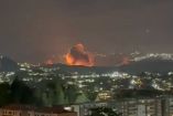 Vista nocturna de Caracas con una gran explosión e incendio al fondo del valle, visible desde zonas residenciales elevadas, en medio de reportes de fuertes detonaciones y ruidos de aeronaves durante la madrugada.