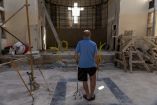 Hombre cristiano caminando con muletas dentro de una iglesia dañada en proceso de reconstrucción en Siria, con andamios y una cruz iluminada al fondo, símbolo de la persecución religiosa y la violencia sufrida por esta comunidad.
