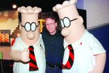 FILE PHOTO: Scott Adams, the creator of "Dilbert", the cartoon character that lampoons the absurdities of corporate life, poses with two "Dilbert" characters at a party January 8, 1999 in Pasadena. The party celebrated the new half-hour animated series "Dilbert", which  debuts on the UPN television network January 25./File Photo