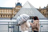 Dos turistas admiran el museo del Louvre desde afuera.