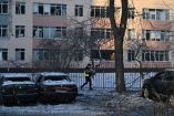 Un policía pasa junto a coches dañados frente a una escuela con ventanas rotas en el lugar donde cayeron restos de drones rusos durante un ataque aéreo ruso a gran escala en Kiev el 20 de enero de 2026.