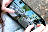 Manos de una menor sostienen un teléfono móvil mientras juega Roblox. En la pantalla se observan avatares y escenarios del videojuego, con chat activo, en un entorno exterior, lo que ilustra el uso cotidiano de la plataforma por niños y niñas.
