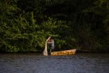 Pescador de pie en una pequeña embarcación lanza una red de pesca en el Río Usumacinta, rodeado de vegetación exuberante y hábitat natural en Chiapa de Corzo, Chiapas, reflejando la vida cotidiana y la biodiversidad del río.
