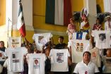 Integrantes de colectivos de desaparecidos levantan playeras con fotografías y fichas de búsqueda durante el Grito de Independencia encabezado por Rocío Nahle en Plaza Lerdo, Xalapa, mientras al fondo se observa la bandera de México y el acto oficial.
