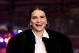 Juliette Binoche sonríe en la alfombra roja del estreno de “Queen at Sea” en la 76ª Berlinale, en Berlín, con abrigo oscuro y camisa blanca, durante la presentación oficial de la película en competencia.