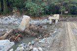 Estructura de concreto de un puente destruido sobre un río con agua lodosa, rodeado de piedras, troncos y escombros arrastrados por la corriente, en zona rural de Chapula, Tianguistengo, tras el huracán Priscilla.