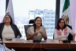 Funcionarias del gobierno federal sentadas en mesa de trabajo durante reunión sobre el Plan de Justicia San Quintín, con banderas institucionales al fondo.