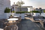 Rooftop con mesas, sillones y jardineras en edificio residencial contemporáneo de la colonia Roma, con pérgola blanca y vista urbana en Ciudad de México.