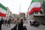 Una enorme bandera iraní ondea en un edificio mientras los iraníes caminan junto a las estructuras dañadas