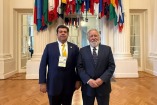 Pedro Haces Barba posa junto a representante internacional en sede de la OEA en Washington, bajo banderas de países miembros durante agenda sobre democracia.