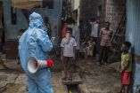 Trabajador sanitario con equipo de protección informa a familias en India durante la pandemia de covid-19 en un barrio urbano con población infantil.