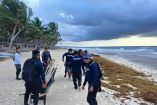 Elementos de la Secretaría de Marina recolectan sargazo en una playa de Quintana Roo con herramientas y carretillas frente al mar.