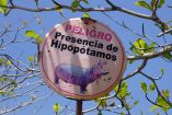 Señal circular con advertencia de peligro por presencia de hipopótamos en Colombia, colocada entre árboles en zona natural bajo cielo despejado.