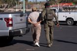 Un inmigrante documentado detenido por el Servicio de Inmigración y Control de Aduanas de Estados Unidos (ICE), camina esposado mientras un agente lo sujeta del brazo en el estacionamiento de un Home Depot en Tucson, Arizona.