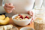 Tazón con avena, rodajas de plátano y fresas, acompañado de frutos secos y miel, preparado como desayuno energético sobre mesa de madera.