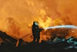 Bombero con manguera combate incendio entre escombros tras explosión en fábrica de fuegos artificiales en Liuyang, Hunan, China.