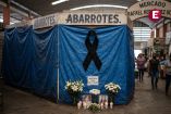 Un primer plano sombrío de un puesto de abarrotes cerrado cubierto con lonas azules en el Mercado Rafael Hernández Ochoa en Cosoleacaque, Veracruz. Un gran lazo negro de luto cuelga en el centro. Debajo, un altar con velas encendidas, flores blancas y dos fotos enmarcadas de las víctimas, Ana Lilia González Mateos y su hija Yalina Lezama.