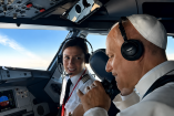 El papa León XIV con auriculares conversa con una piloto en la cabina de un avión durante el trayecto entre Madrid y Barcelona.