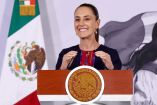Una fotografía de primer plano de Claudia Sheinbaum, Presidenta de México, sonriendo ampliamente detrás del podio oficial del Gobierno de México con el Sello Nacional visible, vistiendo un traje oscuro con bordados de colores. La bandera nacional y un diseño artístico de fondo son visibles