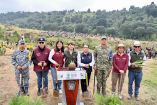 Autoridades y participantes posan durante una jornada de reforestación en una zona forestal del Estado de México junto a árboles y herramientas de campo.
