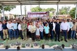 Autoridades, productores y habitantes participan en una entrega de apoyos agrícolas con plantas e insumos colocados frente al grupo.