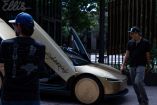 Personas observan un Tesla Cybercab dorado estacionado frente a un bar en el centro de Austin, Texas, con una puerta abierta.