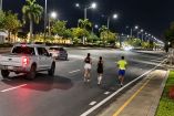 Tres corredores avanzan por una vialidad de Guayaquil de madrugada mientras una camioneta circula detrás del grupo.