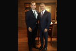 Dos funcionarios posan de pie durante una reunión en un despacho, ambos vestidos con traje y corbata frente a un librero.cue harfuch
