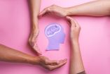 Figura de cabeza con un cerebro ilustrado, rodeada por manos que representan apoyo y cuidado de la salud mental.