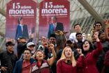 Simpatizantes de Morena levantan los puños frente a lonas por el aniversario 15 del movimiento, con imágenes de Claudia Sheinbaum y Andrés Manuel López Obrador.