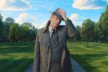 Paul Bettany como Vision en apariencia humana, con sombrero gris, traje y gabardina, en un parque de césped verde.