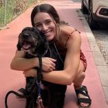 Mujer joven sonriente abraza a un perro negro de tamaño mediano-grande con canas en el hocico y mancha blanca en el pecho, en una acera. Es Boro, perro desaparecido tras el accidente ferroviario en Adamuz, Córdoba.