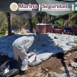 Perito con traje de protección inspecciona costales de precursores químicos bajo una lona en un mega laboratorio desmantelado.