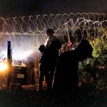 Un grupo de migrantes espera a un costado del muro de púas que divide México de Estados Unidos.