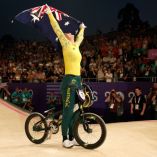 Saya con su bandera y vista hacia el cielo, la bicicleta entre sus piernas con la que es campeona