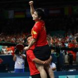 Zhendong con la mano en el aire mientras su entrenador lo carga celebrando la victoria
