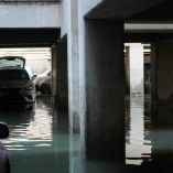 Estacionamiento subterráneo en la colonia Agrícola Pantitlán, Ciudad de México, completamente inundado tras lluvias intensas. Varios autos, con cofres abiertos y marcas de agua, permanecen sumergidos a media altura mientras un trabajador de la alcaldía realiza labores de desazolve.