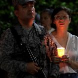 Mujer con blusa blanca sostiene una vela encendida junto a un soldado de la Fuerza Aérea Colombiana durante una vigilia nocturna en memoria de las víctimas del atentado con camión bomba ocurrido en Cali el 24 de agosto de 2025, que dejó seis muertos y más de 60 heridos.