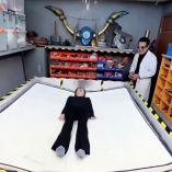 Prototipo de cama antisísmica en funcionamiento con dos personas acostadas sobre la superficie dividida del colchón, en un taller equipado con herramientas, como parte de una demostración en video para mostrar cómo el sistema se activa en caso de sismo.