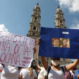 Manifestantes en Tabasco sostienen carteles con mensajes de justicia y fotos de Octavio Ocaña durante una protesta pacífica frente a una iglesia de arquitectura colonial; algunos portan cubrebocas, con cielo parcialmente nublado