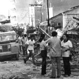 Escena del centro de Managua destruido tras el terremoto de 1972, con edificios colapsados, escombros en la calle y personas recorriendo la zona afectada en medio de la emergencia.