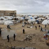 Palestinos desplazados llevan bidones en medio de refugios de tiendas de campaña instalados a lo largo de la costa en la ciudad de Gaza mientras fuertes vientos invernales azotan el enclave palestino el 13 de enero de 2026.