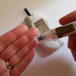 Un persona utiliza su mano y un glucómetro para medir su nivel de azúcar