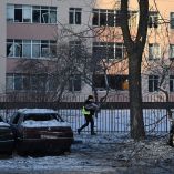 Un policía pasa junto a coches dañados frente a una escuela con ventanas rotas en el lugar donde cayeron restos de drones rusos durante un ataque aéreo ruso a gran escala en Kiev el 20 de enero de 2026.