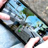 Manos de una menor sostienen un teléfono móvil mientras juega Roblox. En la pantalla se observan avatares y escenarios del videojuego, con chat activo, en un entorno exterior, lo que ilustra el uso cotidiano de la plataforma por niños y niñas.