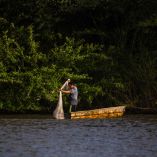 Pescador de pie en una pequeña embarcación lanza una red de pesca en el Río Usumacinta, rodeado de vegetación exuberante y hábitat natural en Chiapa de Corzo, Chiapas, reflejando la vida cotidiana y la biodiversidad del río.