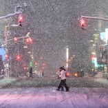 Peatones cruzan una calle en Times Square, Manhattan, bajo fuerte nevada y semáforos en rojo durante una tormenta invernal que impactó Nueva York el 22 de febrero de 2026, con baja visibilidad y acumulación de nieve en la calzada.